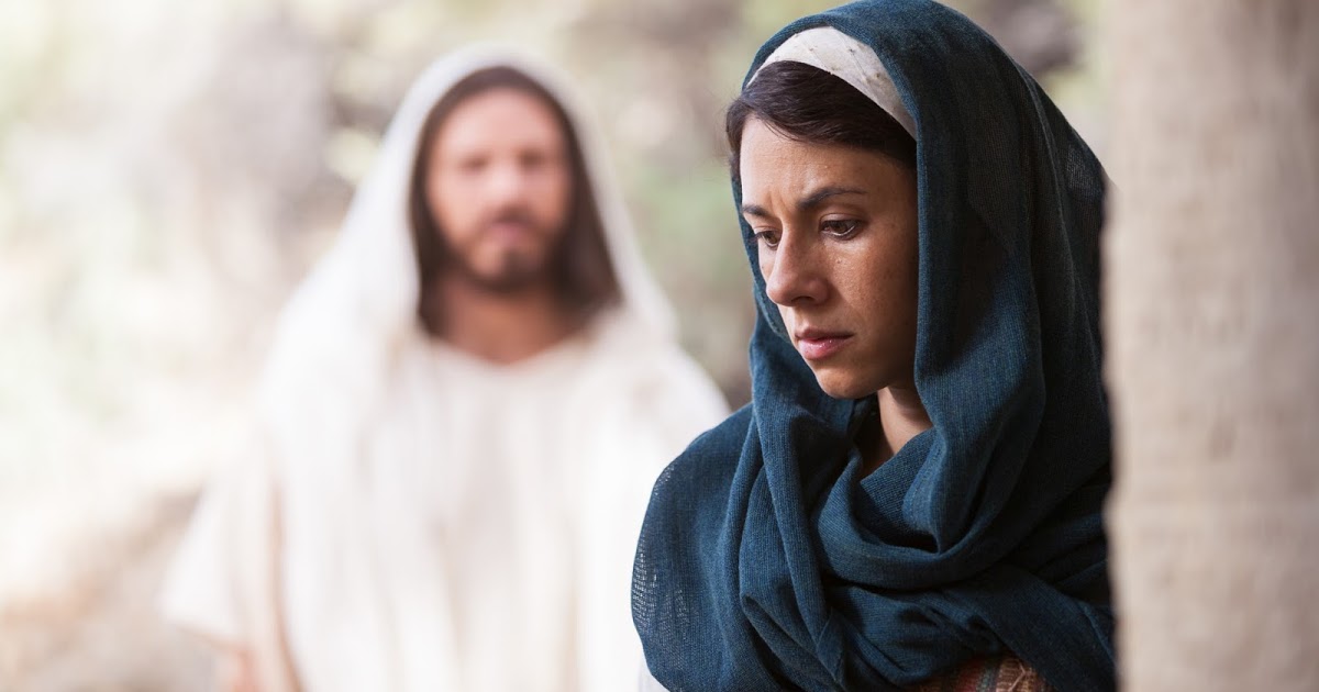 Uma mulher vestida com um manto azul-escuro, identificada como Maria Madalena, está em primeiro plano, com expressão reflexiva. Ao fundo, em desfoque, está Jesus, vestindo túnica branca, observando-a com serenidade. A imagem captura a conexão espiritual entre eles, representando um encontro significativo na narrativa cristã.